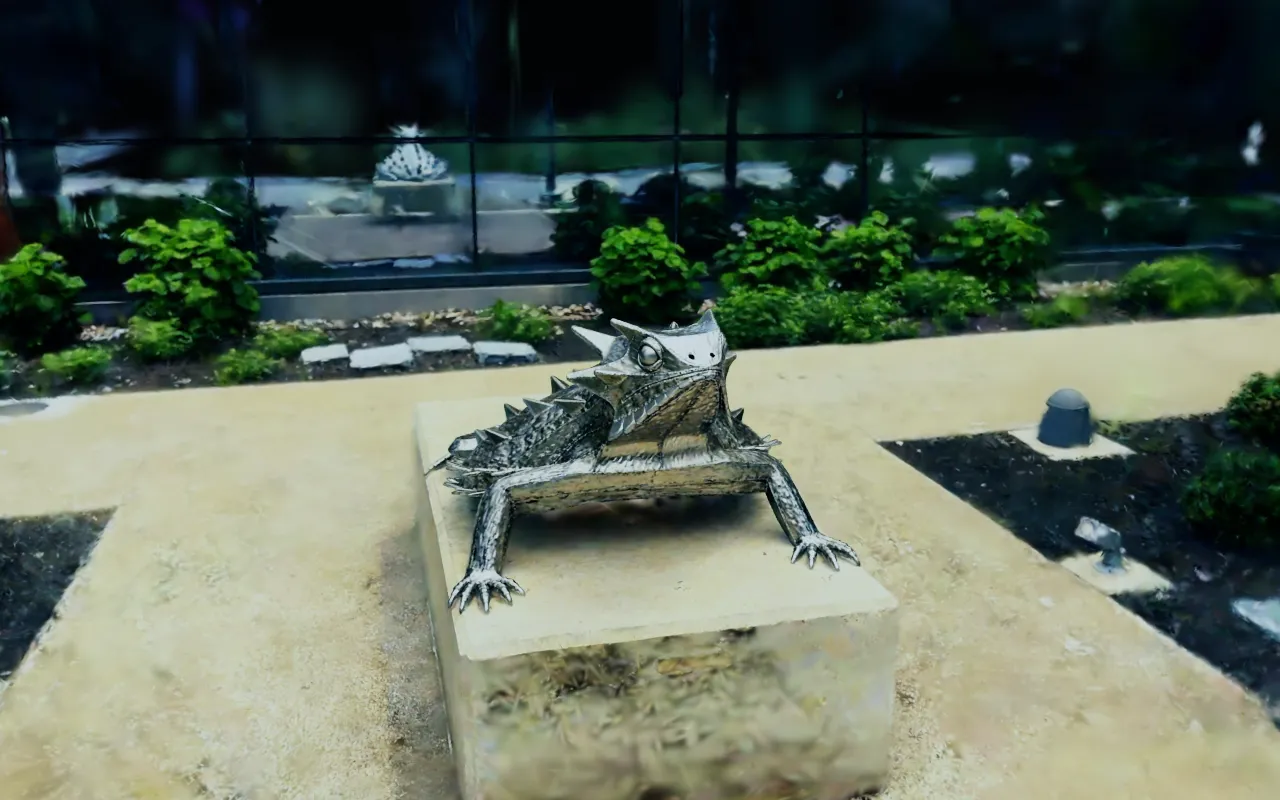 A captured garden: a sculpture on a stone plinth, the path, the planting and a glass building front behind
